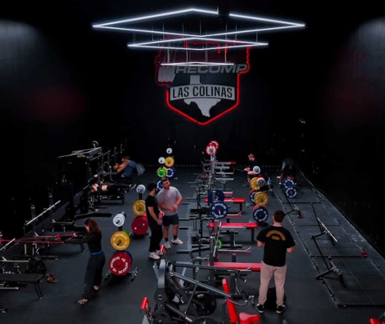 Absolute Recomp Las Colinas powerlifting area with benches and branded wall shield