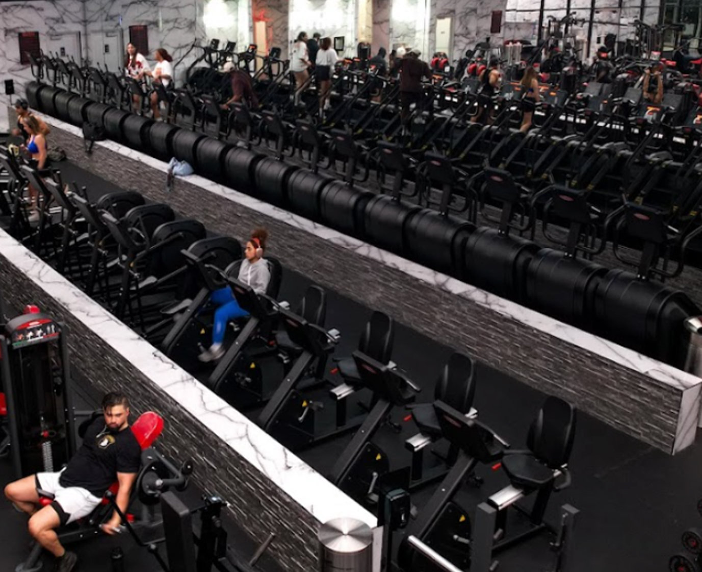 Cardio floor at Absolute Recomp Las Colinas with rows of stair climbers and exercise bikes
