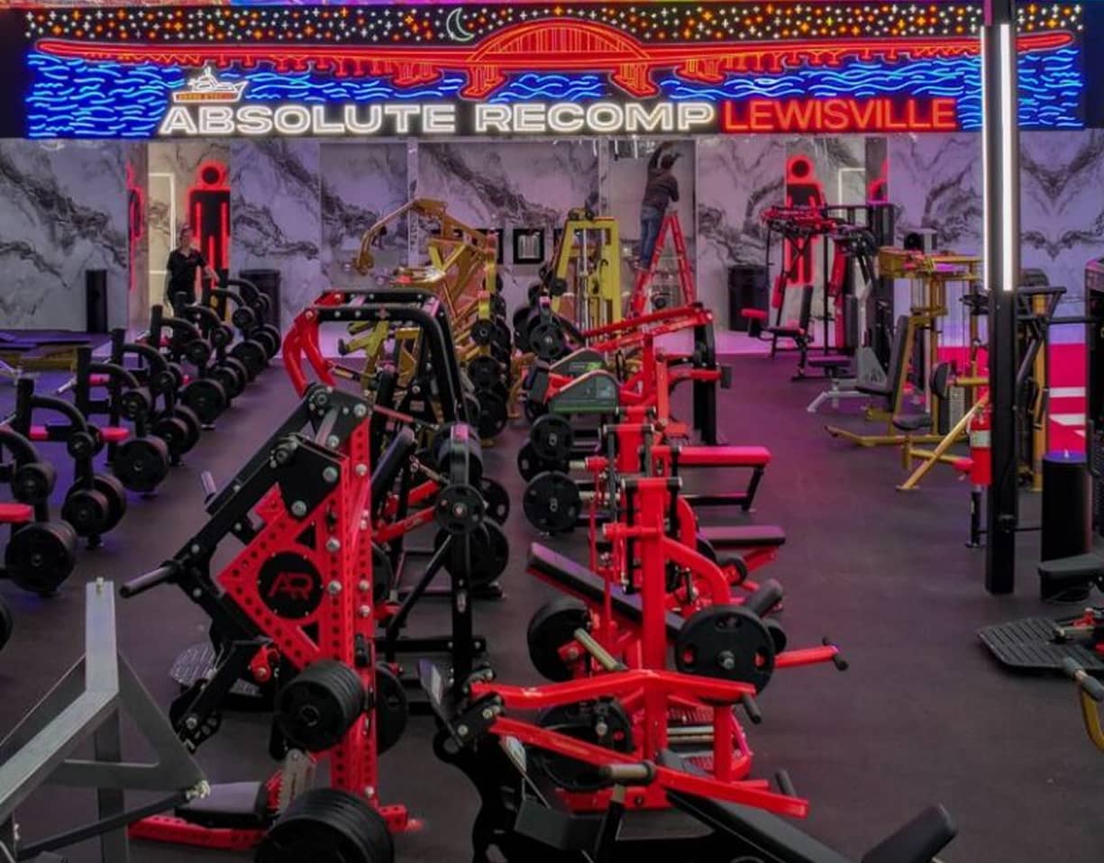 Strength floor at Absolute Recomp Lewisville with branded wall sign and plate-loaded machines