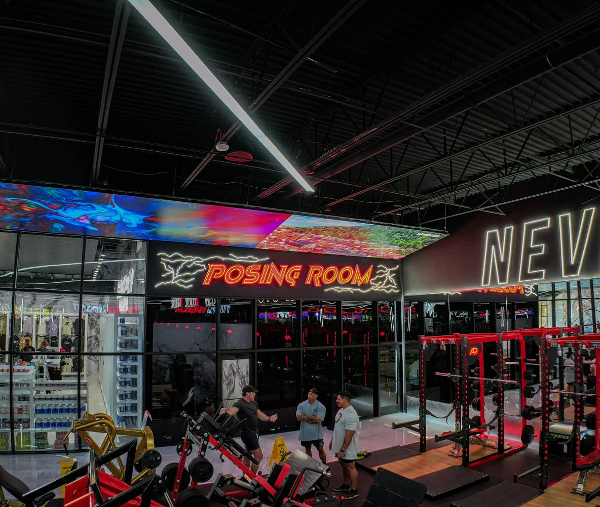 Posing room entrance at Absolute Recomp Lewisville with illuminated sign and training area
