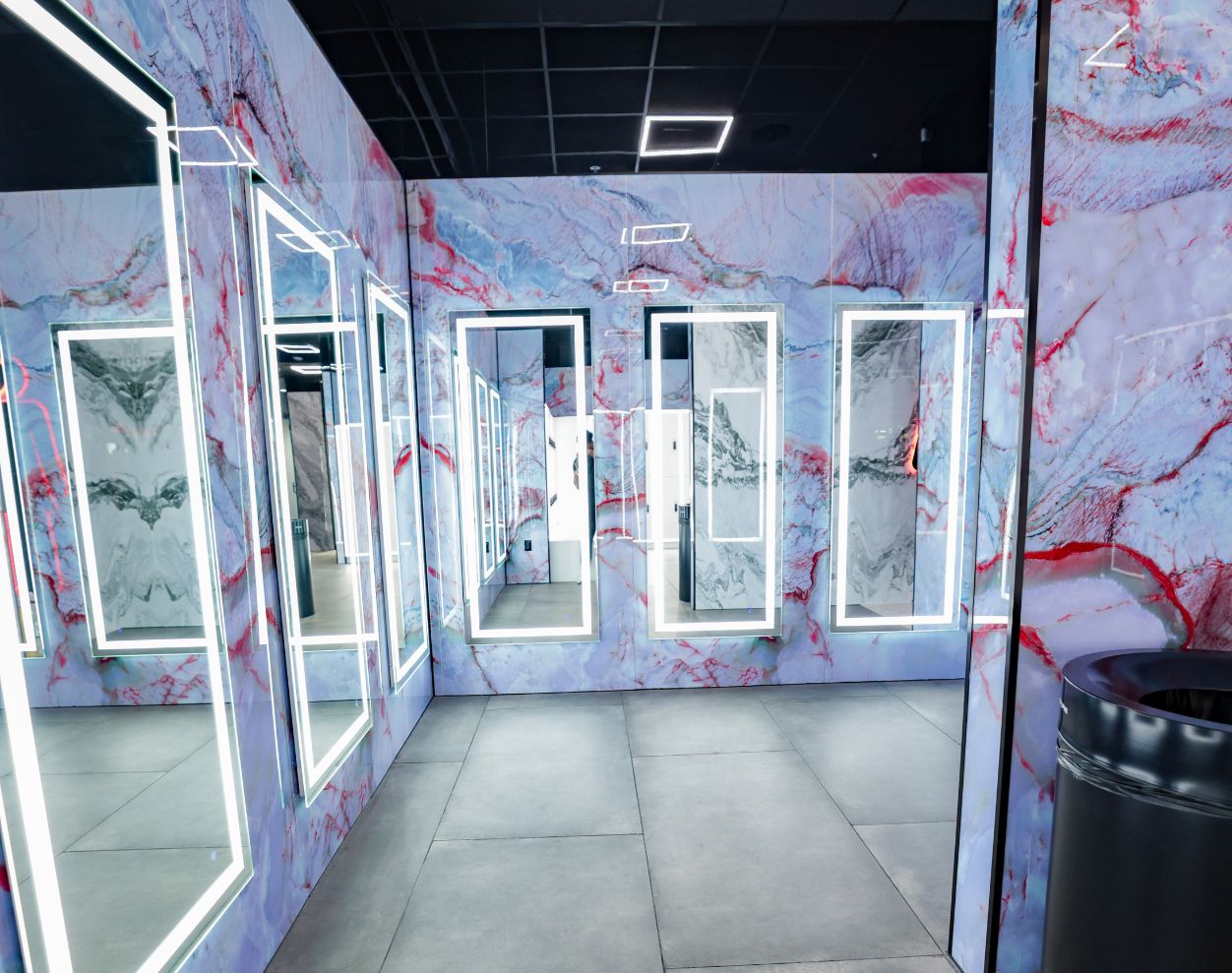 Locker room vanity area with illuminated mirrors and marble-style walls at Absolute Recomp Gyms Lewisville