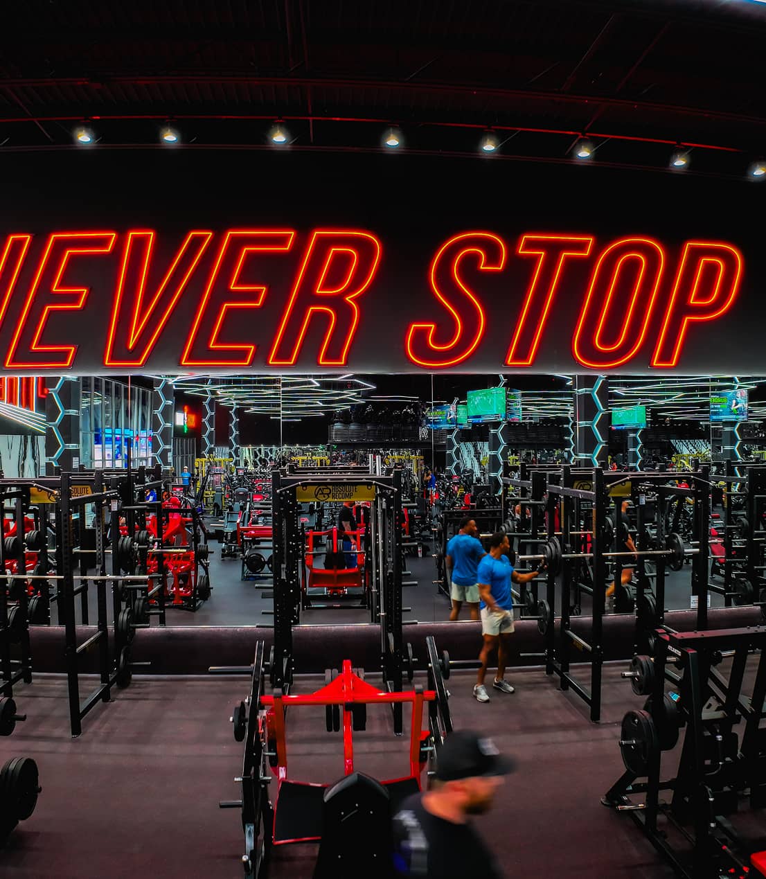 Inside Absolute Recomp gym with weightlifting equipment and “Never Stop” wall sign